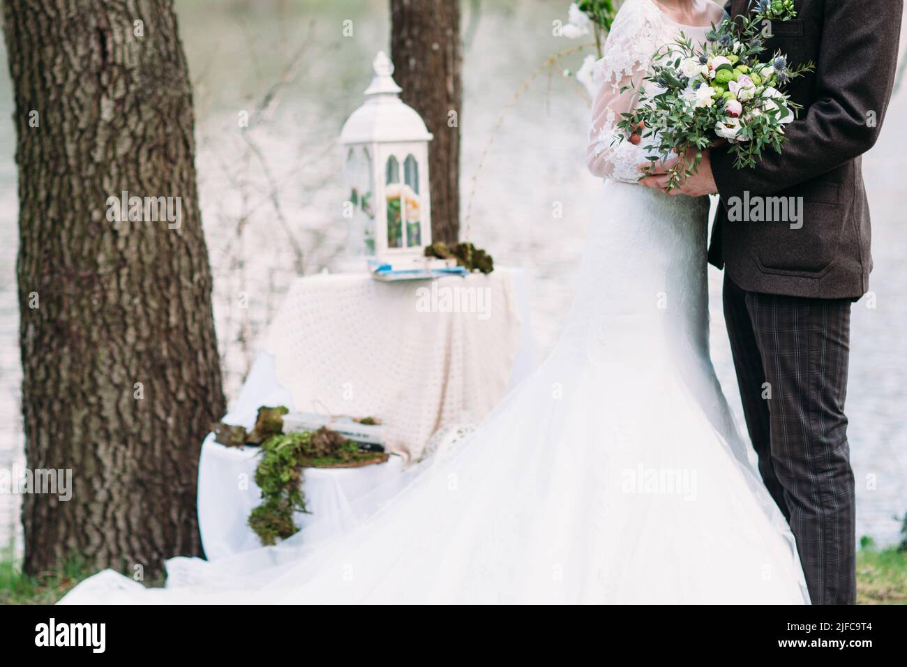 Gerade verheiratetes Paar umarmt sich im Freien mit Blumenstrauß Stockfoto