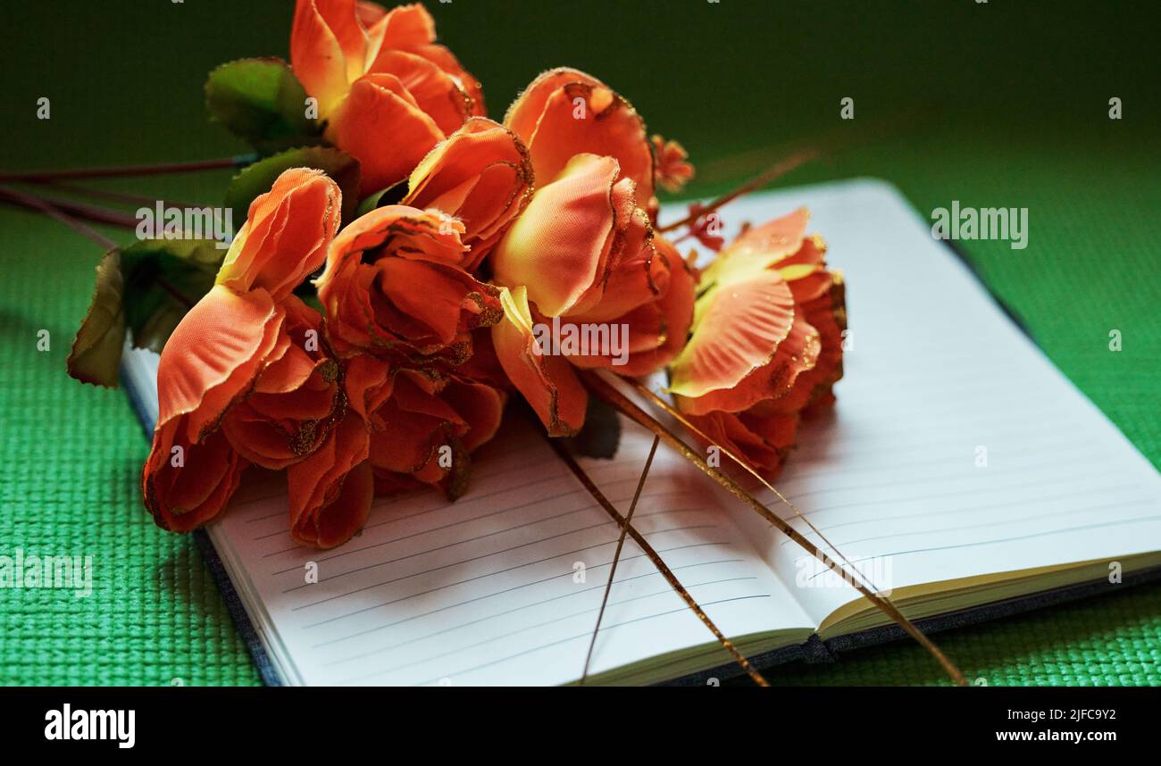 Oben Aufnahme von orangen Blumen auf einem offenen Notizblock. Die Natur kann uns inspirieren zu schreiben und unsere Kreativität zu entfachen. Werden Sie produktiv und motiviert in einer kreativen Stockfoto
