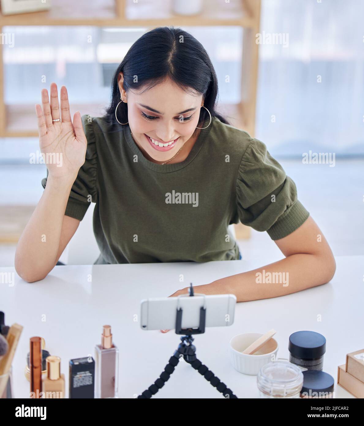 Hispanische Beauty-Bloggerin winkt ihr Smartphone an, während sie ein Video aufzeichnet oder live sendet. Schöne junge Influencerin, die ihre Beauty-Produkte teilt Stockfoto