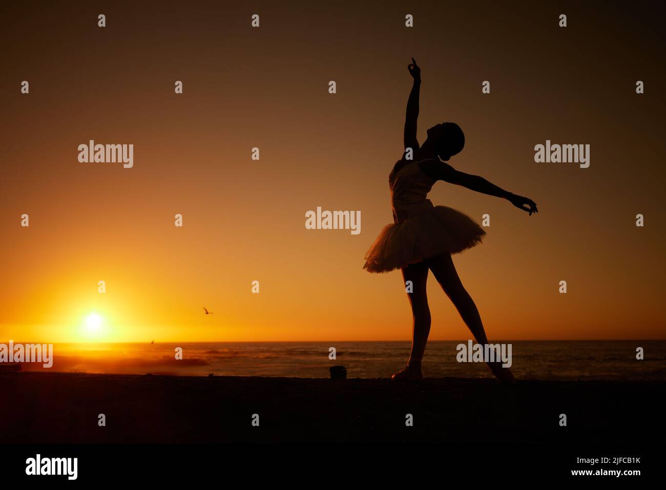 Silhouette einer Balletttänzerin beim Tanzen am Strand bei Sonnenuntergang. Anmutige schlanke Ballerina, die im Freien tanzt Stockfoto