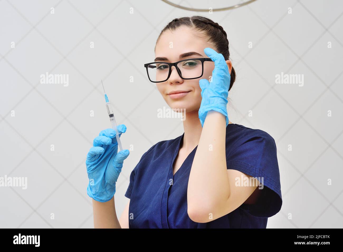 Junge Frau in einem OP-Anzug und einer Brille mit einer Spritze in den Händen Stockfoto