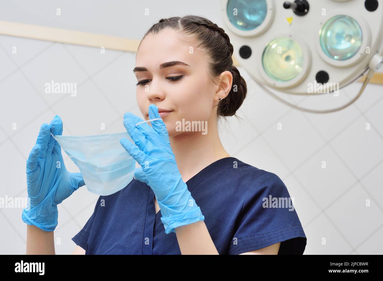 Hübsche junge Frau in einem OP-Anzug zieht eine sterile Maske an. Stockfoto