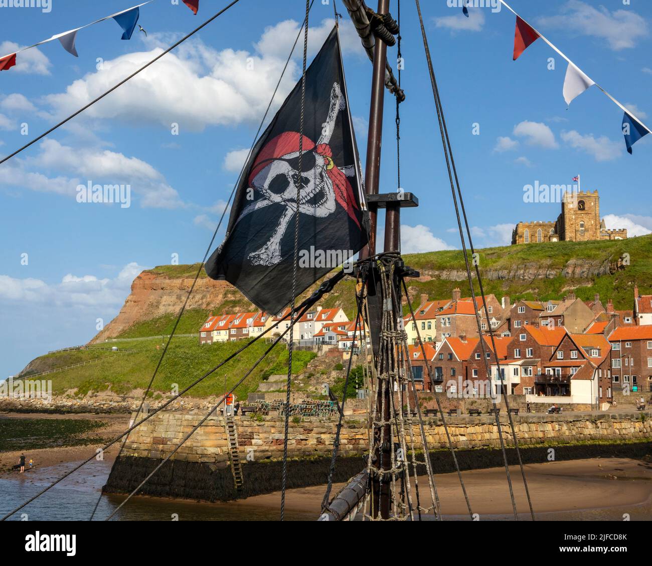 Whitby, Großbritannien - 10. 2022. Juni: Die Jolly Rodger-Flagge auf einem Piratenschiff in Whitby Harbour in North Yorkshire, Großbritannien. St. Marys Kirche kann in gesehen werden Stockfoto