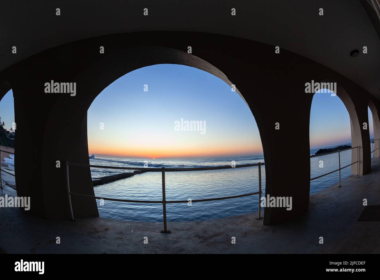 Gezeitenpool am Strand durch die Bögen am frühen Morgen des Sonnenaufgangs über dem Ozeanhorizont. Stockfoto