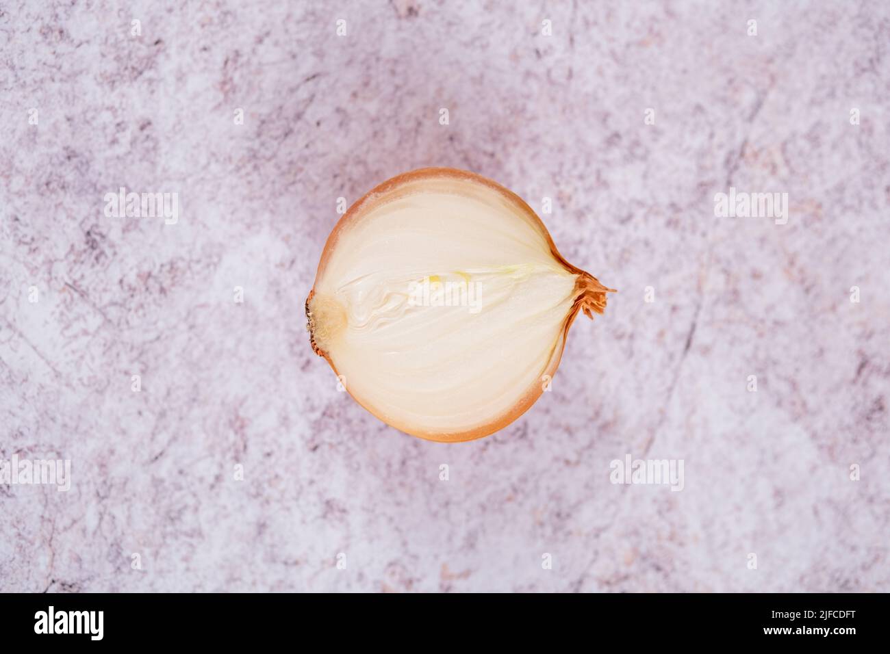 Eine halbierte weiße Zwiebel mit Haut auf, vor einem Hintergrund aus weißem Stein. Stockfoto