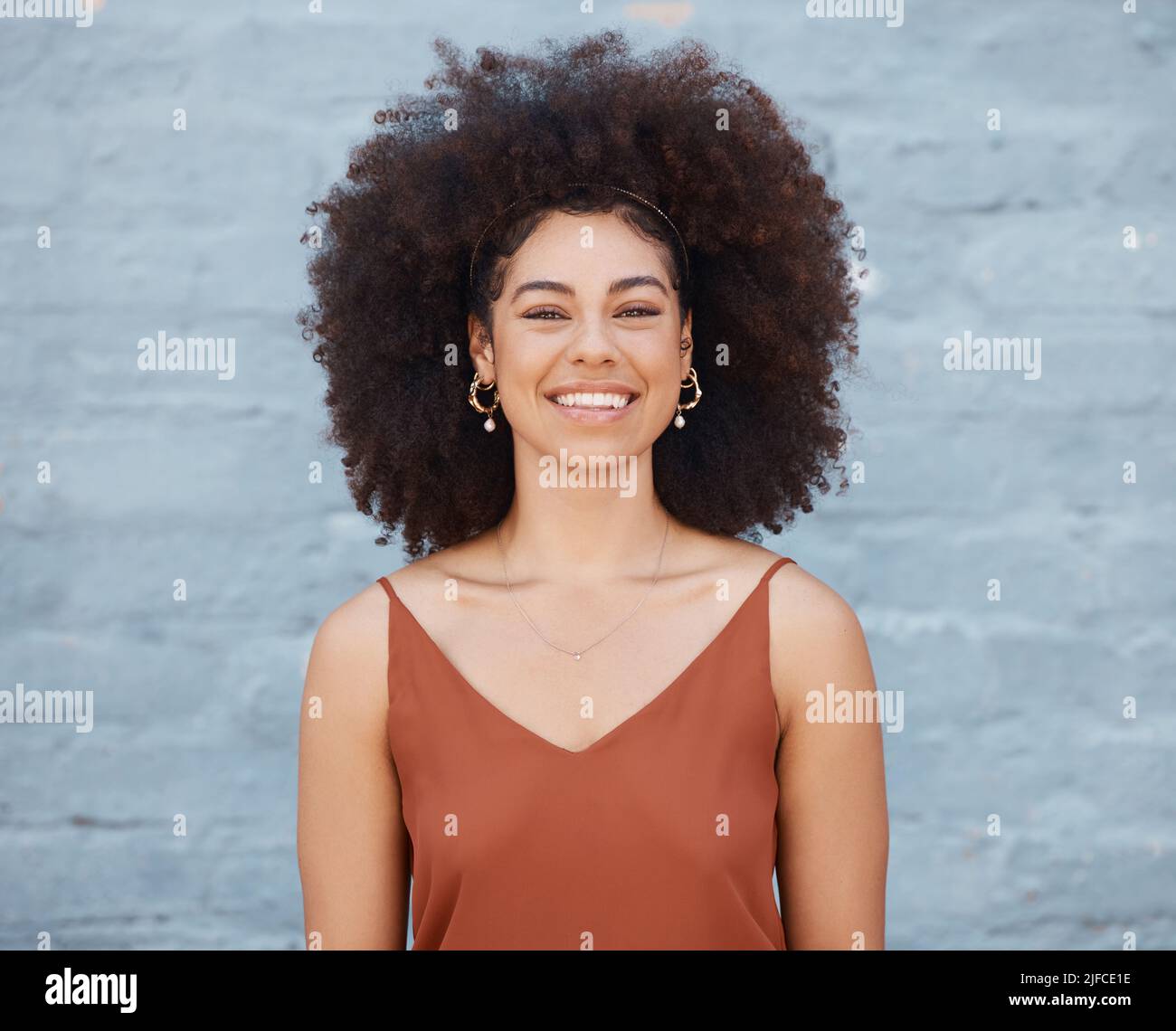 Porträt einer fröhlichen Frau mit großem Afro und einem schönen Lächeln, das draußen vor einer Backsteinmauer steht. Unbeschwerte Frau, die tagsüber draußen posiert Stockfoto