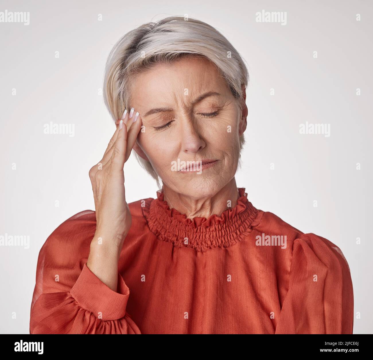 Eine reife Frau, die unter Kopfschmerzen leidet und gestresst aussieht, während sie vor einem grauen Copyspace-Hintergrund posiert. Alternde Frau, die Angst hat Stockfoto