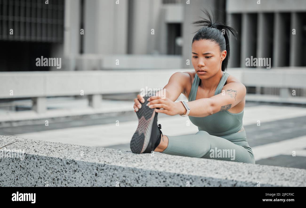 Junge hispanische Athletin mit gemischtem Rennen, die ihr Bein vor einem Lauf in der Stadt streckt. Bewegung ist gut für Ihre Gesundheit und Ihr Wohlbefinden Stockfoto