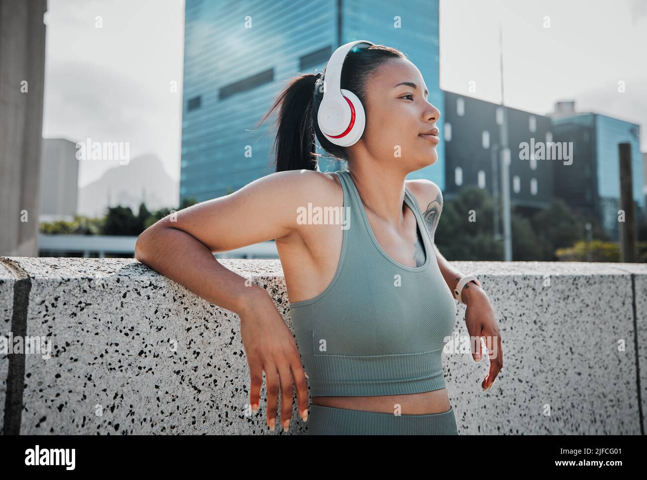 Junge hispanische Athletin mit gemischtem Rennen, die Kopfhörer trägt und Musik hört, während sie draußen in der Stadt steht. Positiv, glücklich, Workout Stockfoto