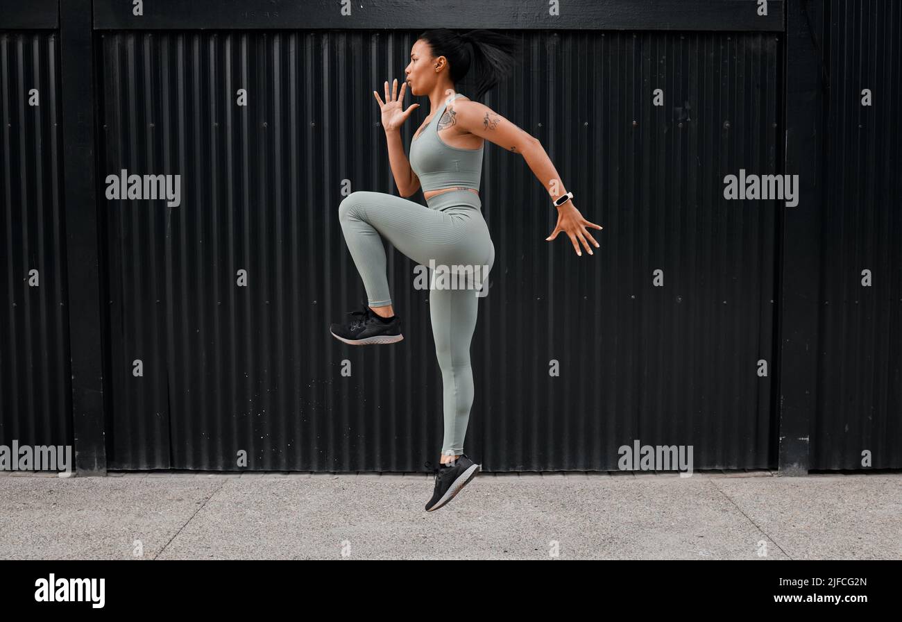 Eine junge afroamerikanische Athletin, die vor Ort läuft, während sie draußen in der Stadt trainiert. Schöne und engagierte Mixed-Race-Sportlerin Stockfoto