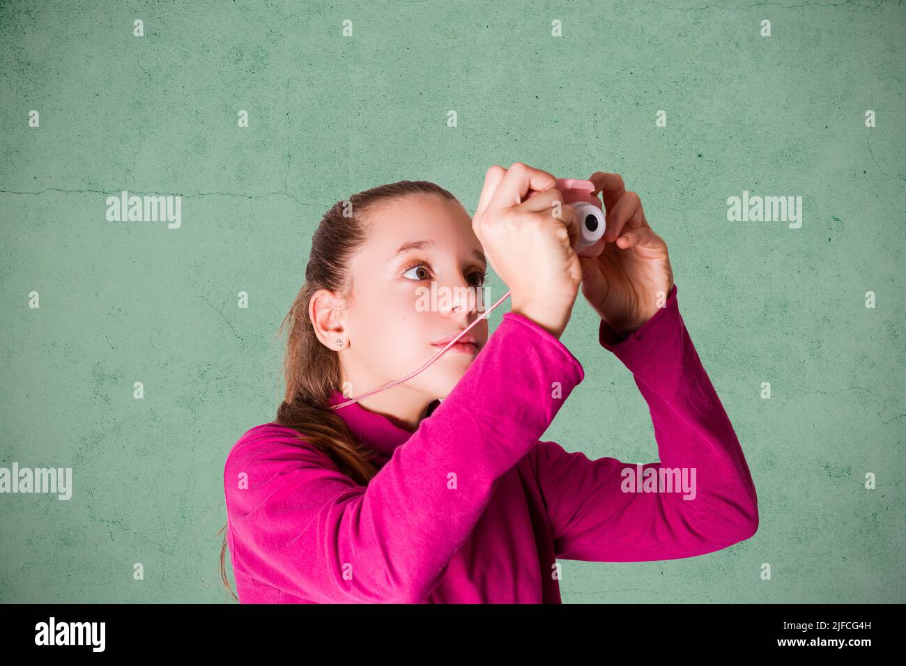 Kleines Mädchen, das Bild mit Spielzeug-Fotokamera auf grünem Hintergrund Stockfoto