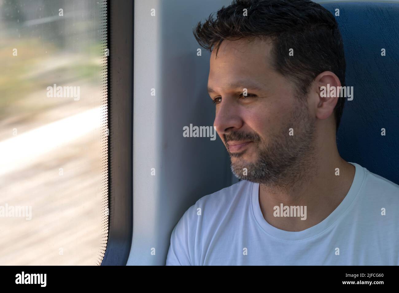 Hispanischer junger Mann in einem Zug, lächelnd und aus dem Fenster blickend Stockfoto