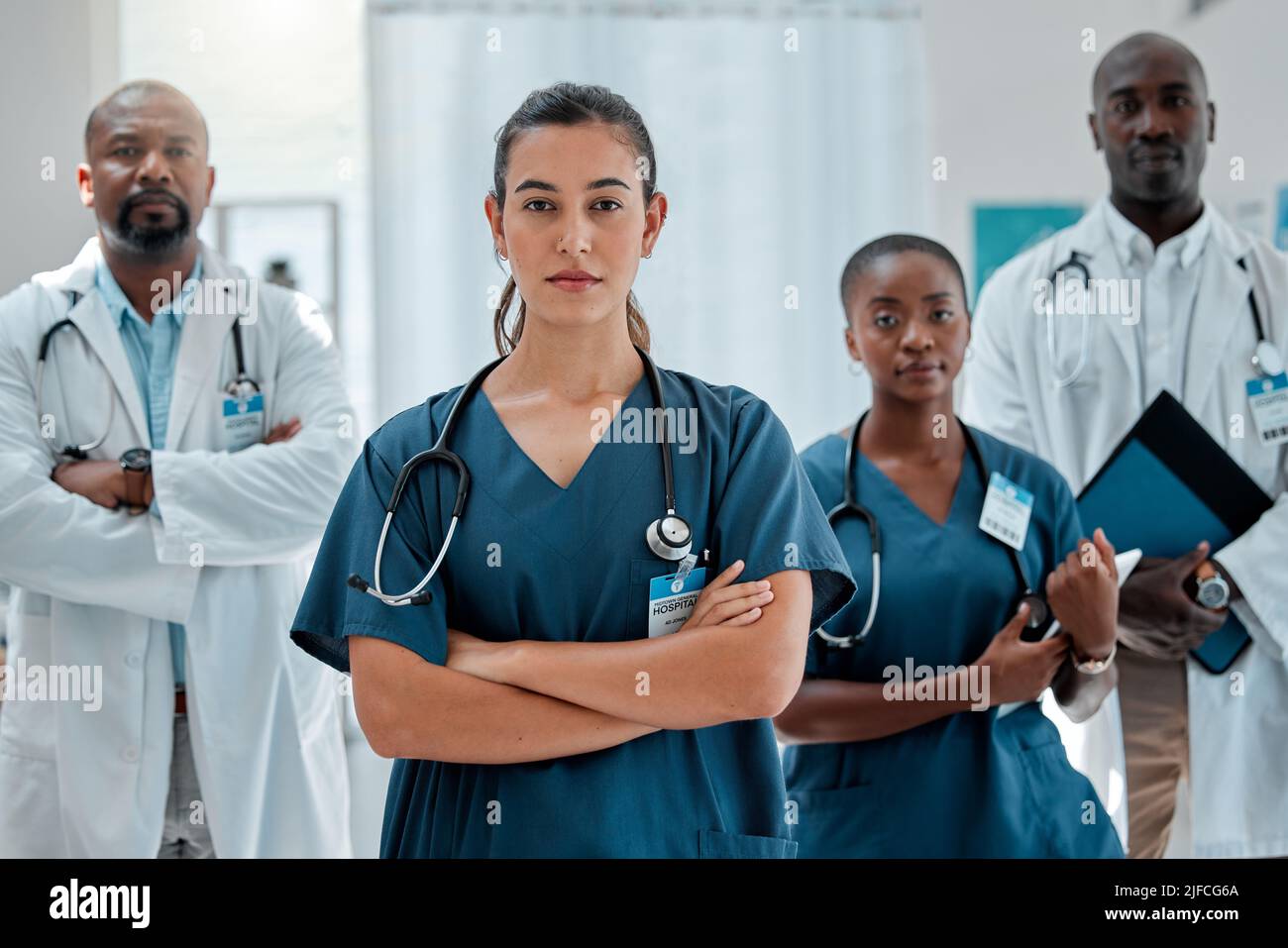 Eine Gruppe ernsthafter verschiedener Ärzte, die während der Arbeit in einem Krankenhaus mit gekreuzten Armen stehen. Fokussierte medizinische Fachkräfte bei der Zusammenarbeit Stockfoto