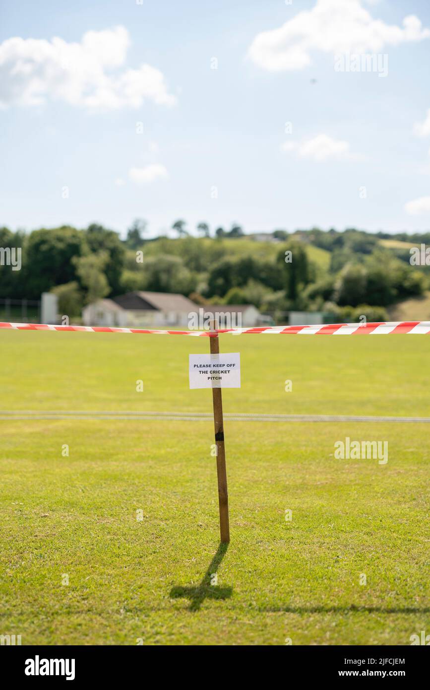 Ein Schild mit der Aufschrift „Bitte halten Sie sich vom Cricket-Platz weg“ mit Warnband in einem ländlichen Dorf. Stockfoto