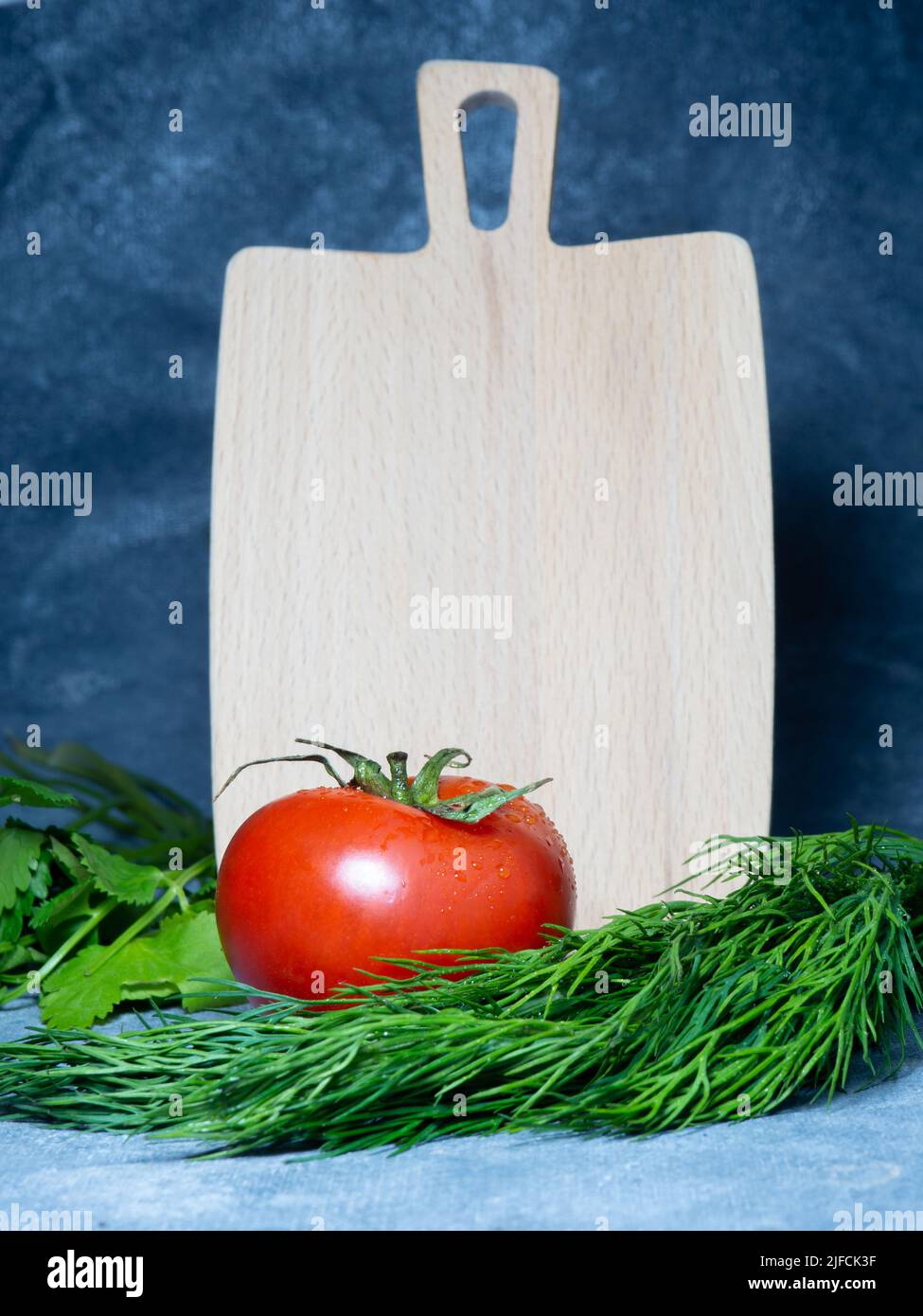 Gewächshaus-Tomate auf einem kleinen Brett. Originalgröße. Tomate in der Küche. Kochen. Reifes frisches Gemüse auf hölzernen Küchenutensilien. Ungewöhnliches Schneiden von bo Stockfoto