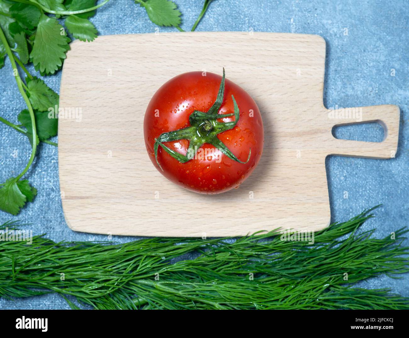 Gewächshaus-Tomate auf einem kleinen Brett. Originalgröße. Tomate in der Küche. Kochen. Reifes frisches Gemüse auf hölzernen Küchenutensilien. Ungewöhnliches Schneiden von bo Stockfoto