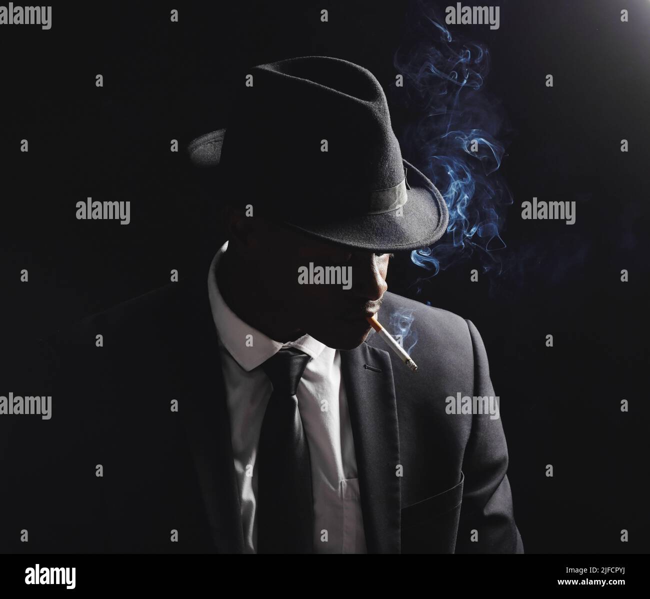 Afroamerikanischer Mann posiert vor schwarzem Hintergrund. Vintage-Hitman in der Mafia sieht beim Rauchen einer Zigarette gefährlich und kantig aus. Modisch Stockfoto