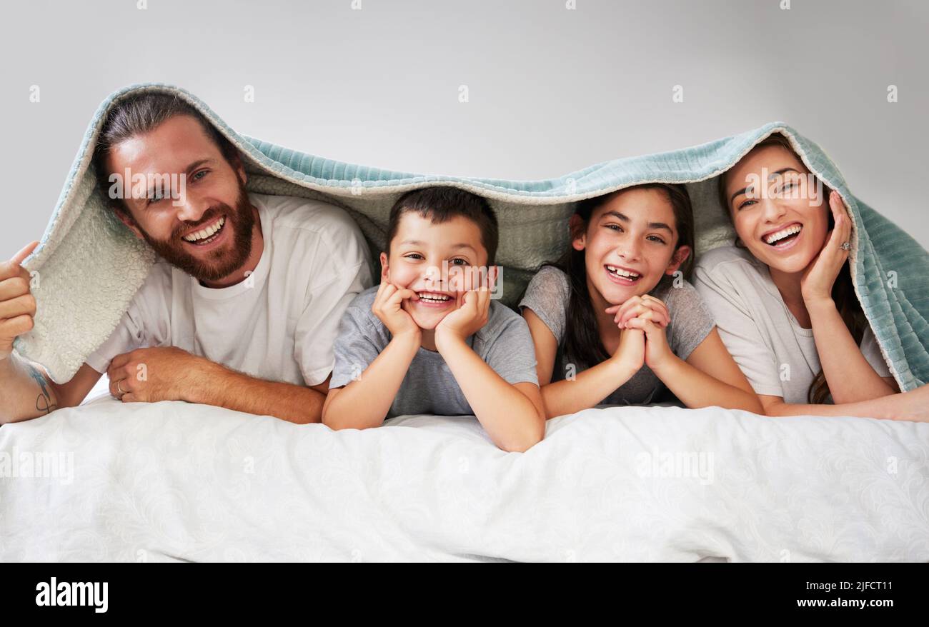 Porträt einer glücklichen vierköpfigen kaukasischen Familie, die mit einer sherpa-Decke über dem Kopf zusammen auf dem Bett lag. Sorglose Eltern verbringen Freizeit mit Stockfoto