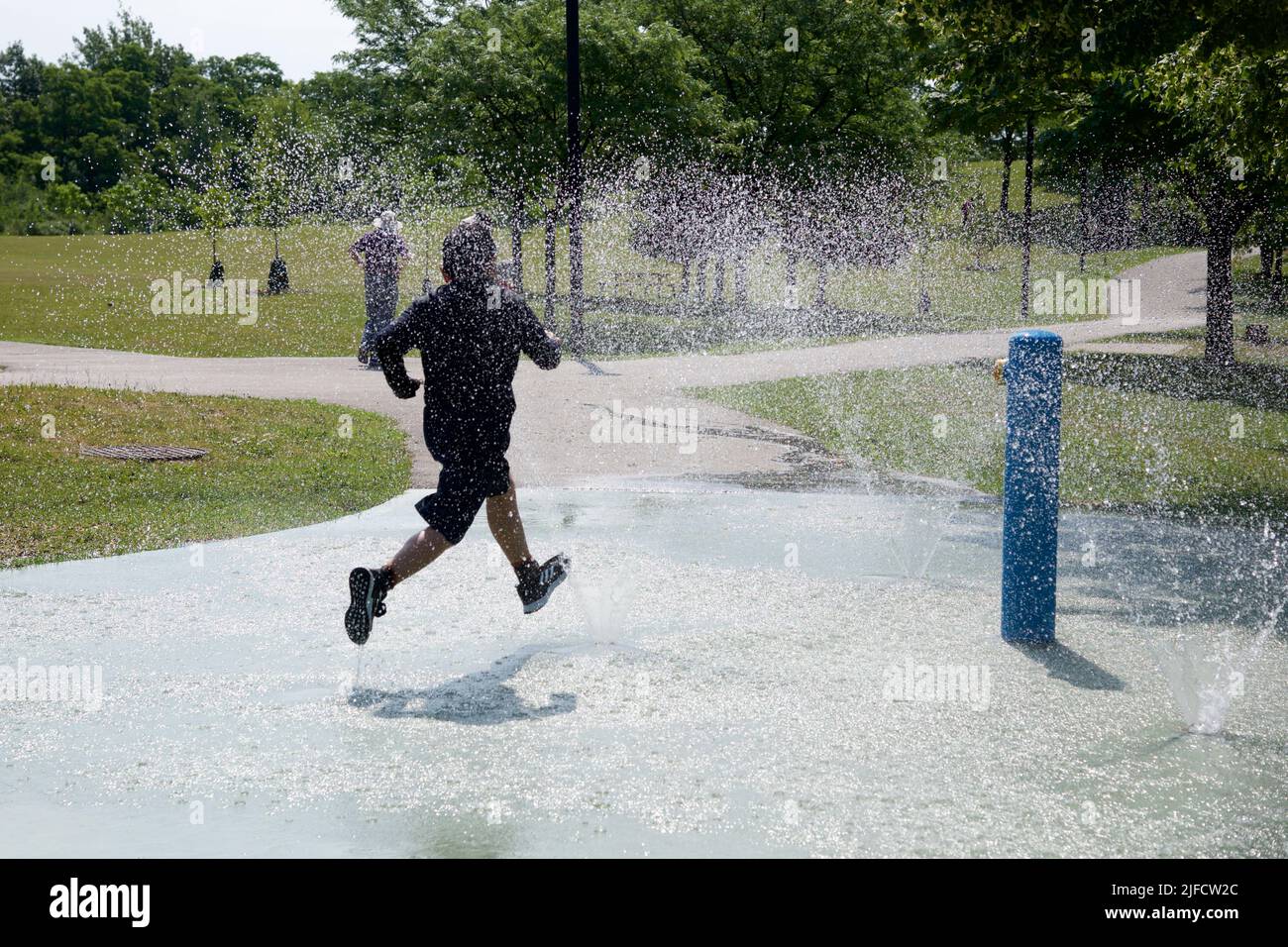 Toronto, Ontario / Canada - 06/30/2022: Junge spielen mit Wasser an einem heißen Sommertag. Junge, der zwischen dem Sprinkler läuft. Spaß im Freien. Stockfoto