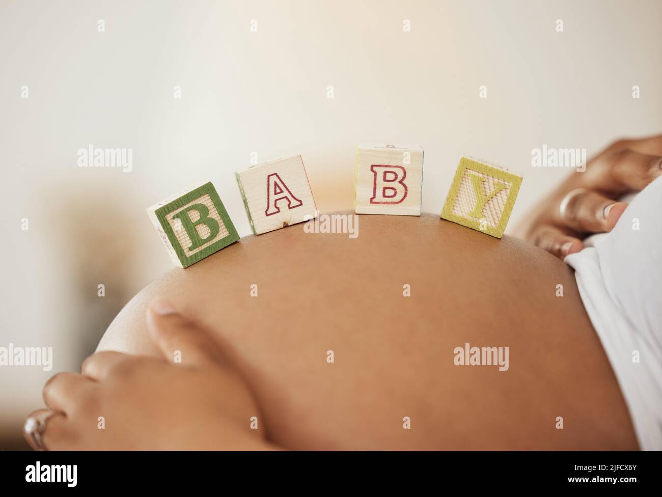 Nahaufnahme einer Schwangeren, die ihren Bauch zeigt, während sie sich mit hölzernen Spielblöcken mit Baby-Schriftzug darauf legt Stockfoto