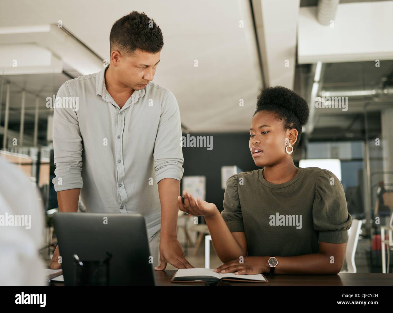 Zwei multiethnische Geschäftsleute sprechen an einem Schreibtisch über Online-Projekte auf einem Laptop. Mentor und Kollege erklären und Ideen mit Brainstorming durchführen Stockfoto