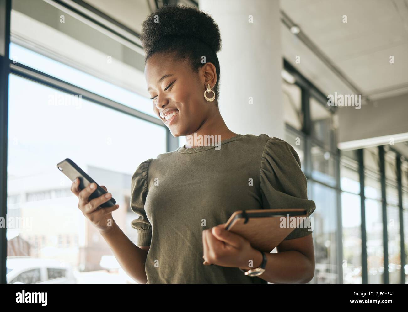 afroamerikanische Geschäftsfrau, die lächelt, während sie auf dem Smartphone liest oder SMS schreibt, Tagebuch hält und im modernen Büro läuft. Lächelnd, weiblich Stockfoto