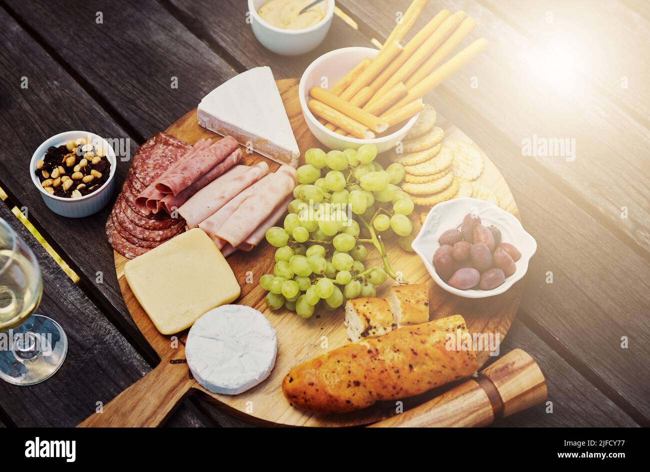 Blick über eine Vielzahl von Snacks auf einem Tapas-Holzbrett draußen. Käse, Brot, frische Trauben und Aufschnitt zum Mittagessen auf einem Weinberg. Essen Stockfoto