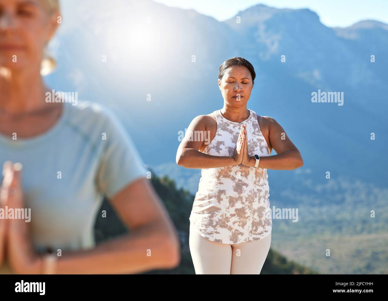 Reife Frau meditiert mit verbundenen Händen und geschlossenen Augen und atmet tief. Reife Menschen machen an einem sonnigen Tag gemeinsam Yoga in der Natur Stockfoto