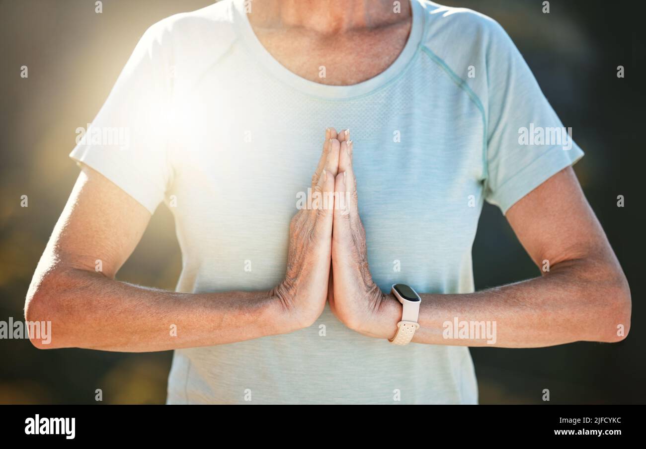 Nahaufnahme einer älteren Frau, die draußen mit verbundenen Händen in namastiger Position steht und in der Natur meditiert. Innere Ruhe, Balance und Leben finden Stockfoto