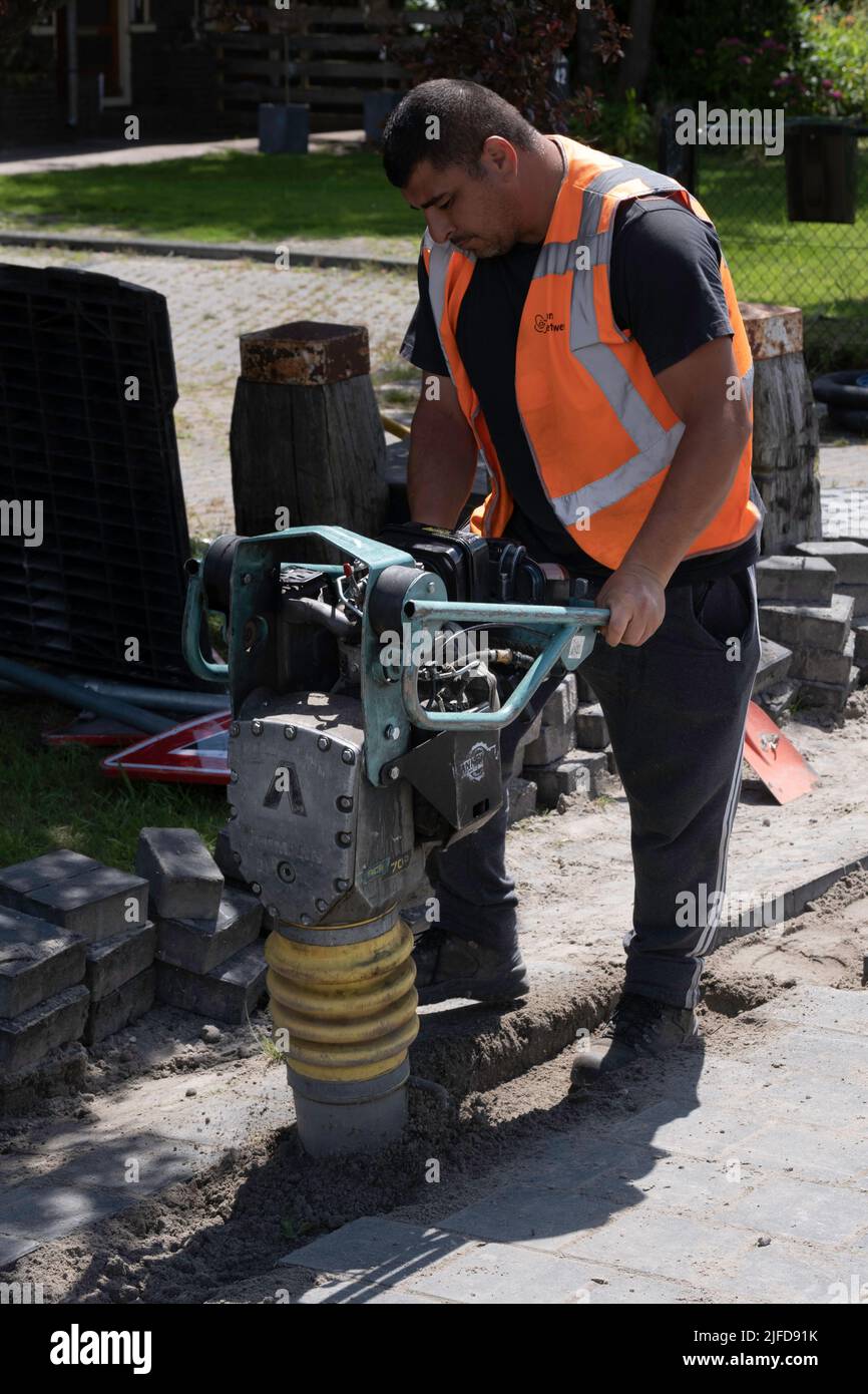 Mitarbeiter der niederländischen Telefongesellschaft KPN arbeitet mit einem tragbaren Schwingungsstamper, um nach dem Verlegen von Kabeln den Sand abzuschleifen. Straßenarbeiten Stockfoto