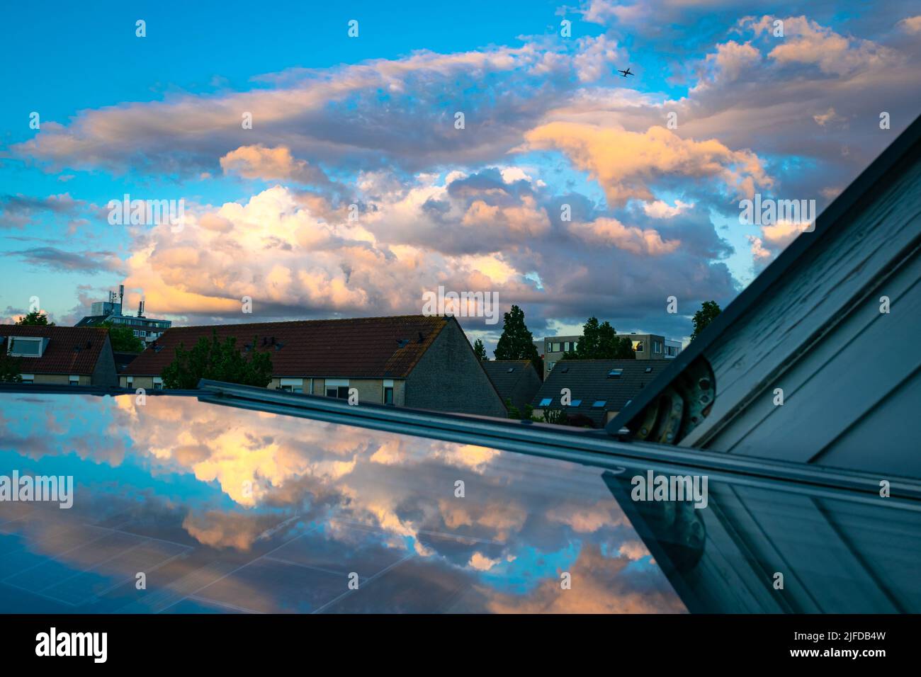 Bunte Cumuluswolken, die von der niedrigen Sonne erleuchtet werden. Die Wolken spiegeln sich im Glas eines Oberlichts. Stockfoto
