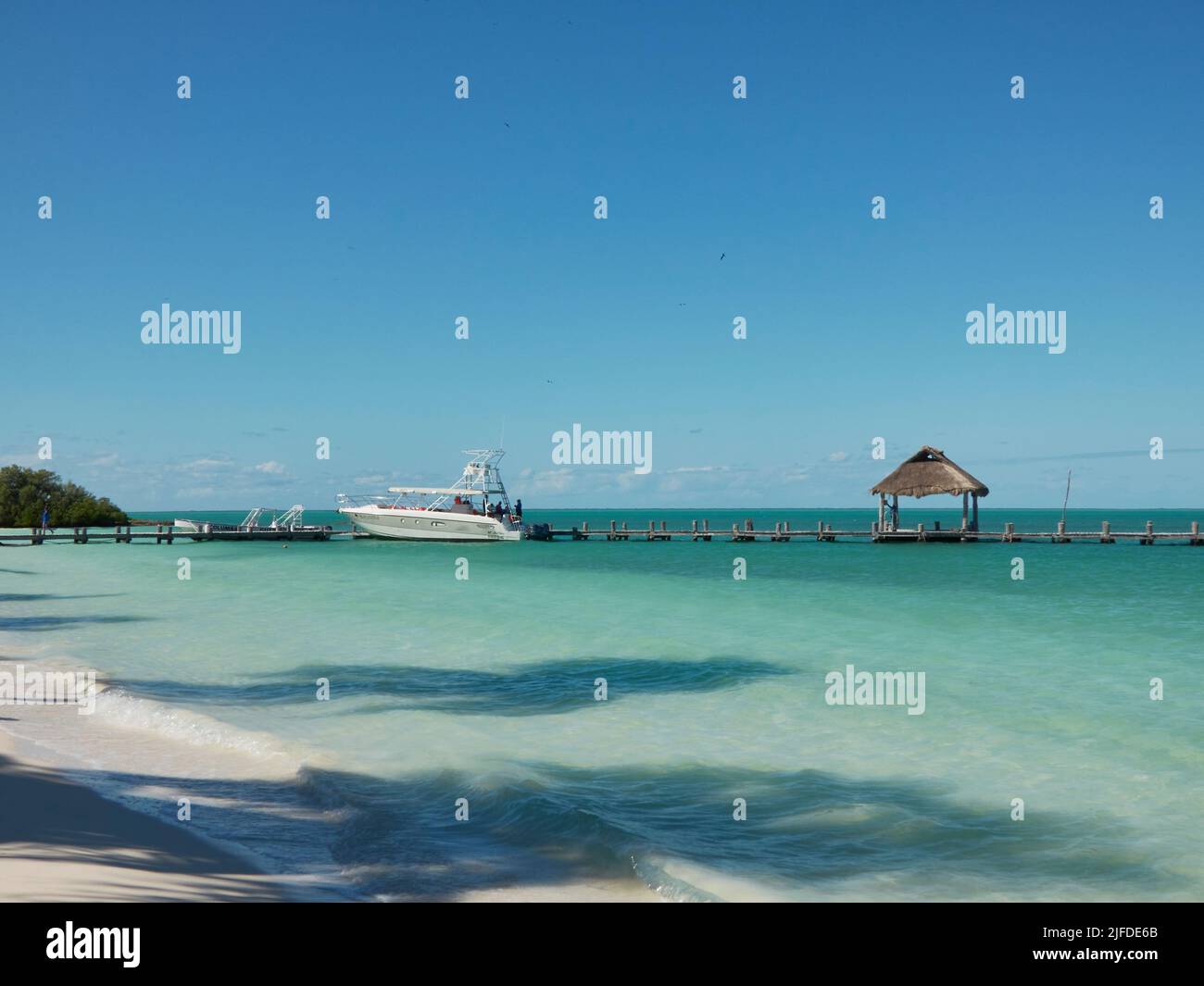 Ein hölzerner Pier an einem paradiesisch leeren Strand mit einer großen Yacht, die in der Nähe geparkt ist Stockfoto