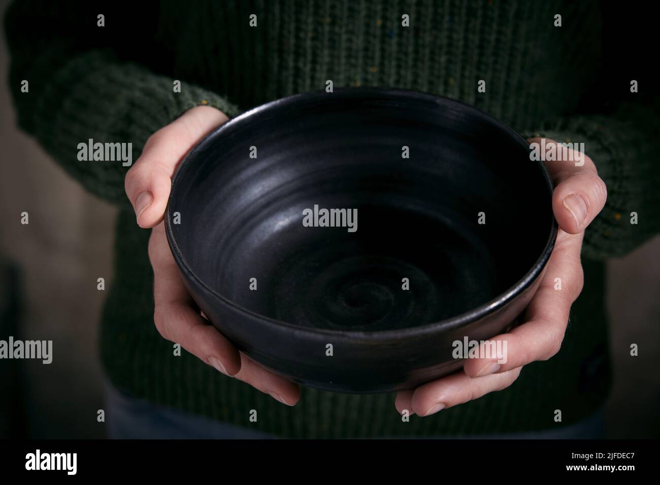 Hoher Winkel der Ernte anonyme Frau in warmen Pullover hält stilvolle leere Keramikschale in den Händen Stockfoto