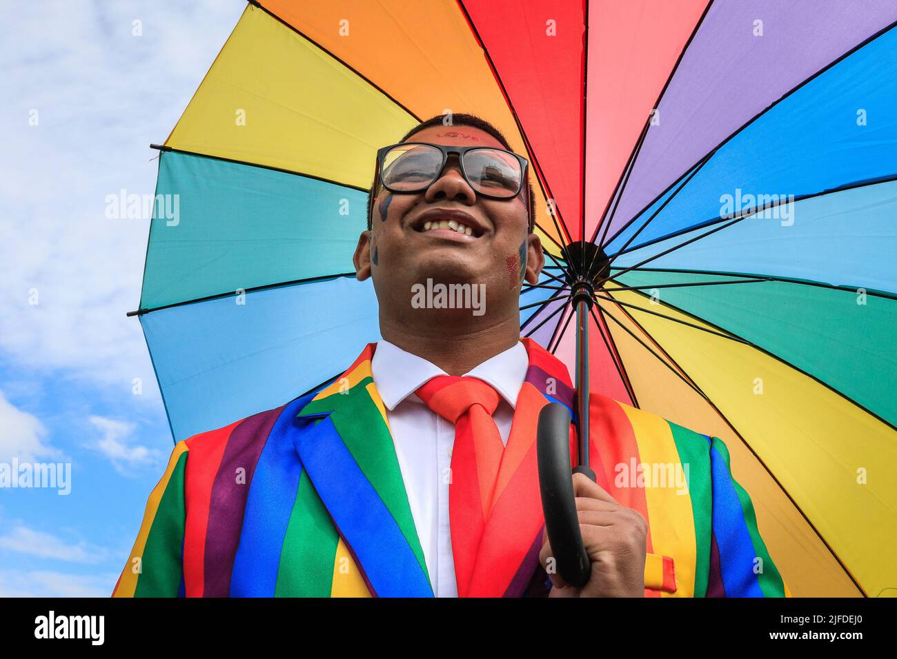 London, Großbritannien. 02.. Juli 2022. Ein Teilnehmer posiert stolz mit dem Regenbogenschirm während des Aufbaus in der Park Lane. Teilnehmer und Zuschauer haben Spaß auf der Route der Pride in London 2022 Parade. Die Parade führt dieses Jahr vom Hype Park entlang Piccadilly nach Whitehall. Die Pride-Bewegung und die LGBT-Gemeinschaft erinnern an 50 Jahre, seit die erste Pride im Vereinigten Königreich stattfand. Kredit: Imageplotter/Alamy Live Nachrichten Stockfoto