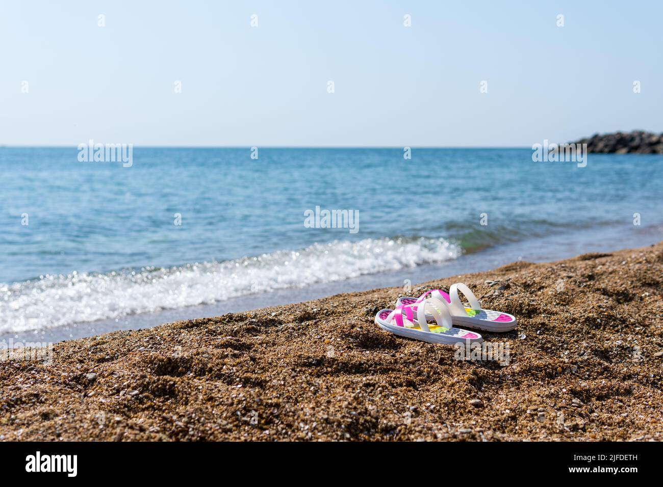 Bunte Flip Flops am sonnigen Sandstrand mit türkisfarbenem Wasser. Inselurlaub am heißen Sommertag. Wunderschöne Meereswellen im Hintergrund. Sommer Stockfoto