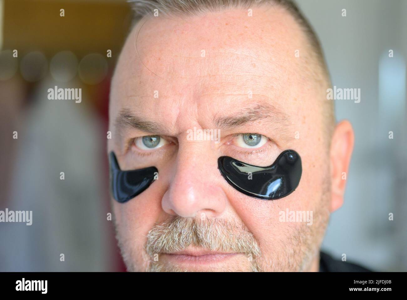 Mann mittleren Alters verwendet Gel-Feuchtigkeitsflecken oder eine Maske auf der Haut unter seinen Augen in einem Anti-Aging-Konzept Stockfoto