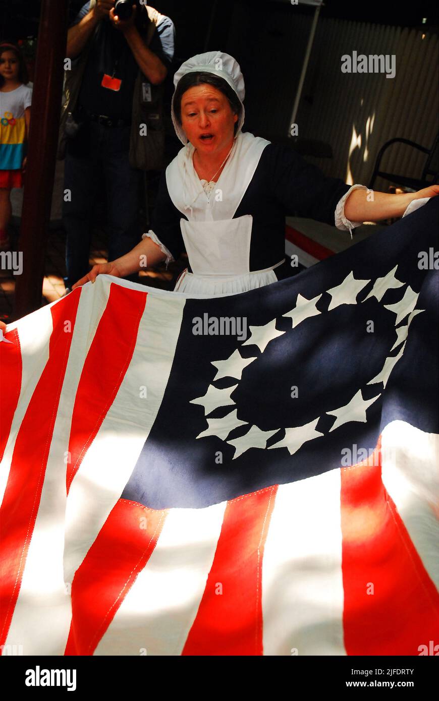 Ein Betsy Ross Reenactor entfaltet eine koloniale amerikanische Flagge, demonstriert die Kunst und den Prozess einer Näherin, die zur Erstellung der Flagge verwendet wurde Stockfoto