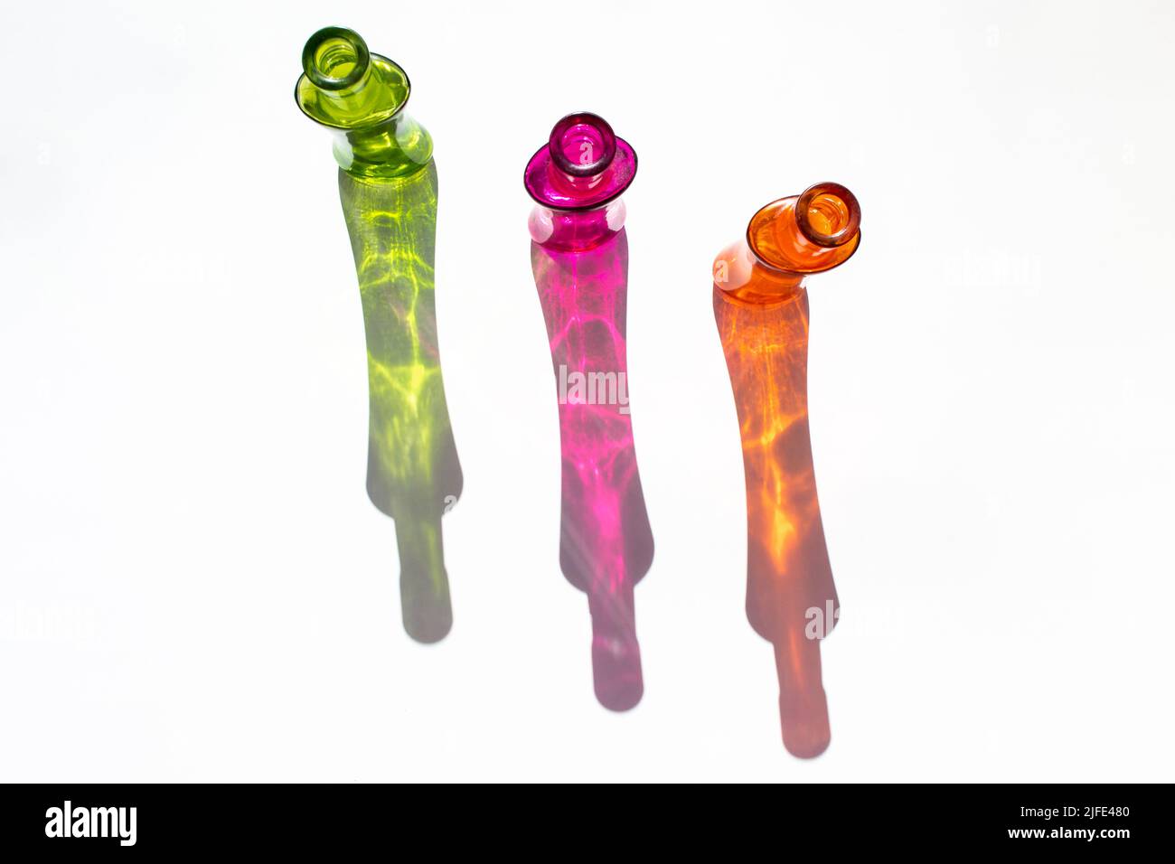 Schöne Glasflaschen grün, orange und rosa. Farbige Flaschenschatten durch Sonnenlicht. Weißer Hintergrund. Innenarchitektur. Abstrakte Wandgestaltung. Stockfoto