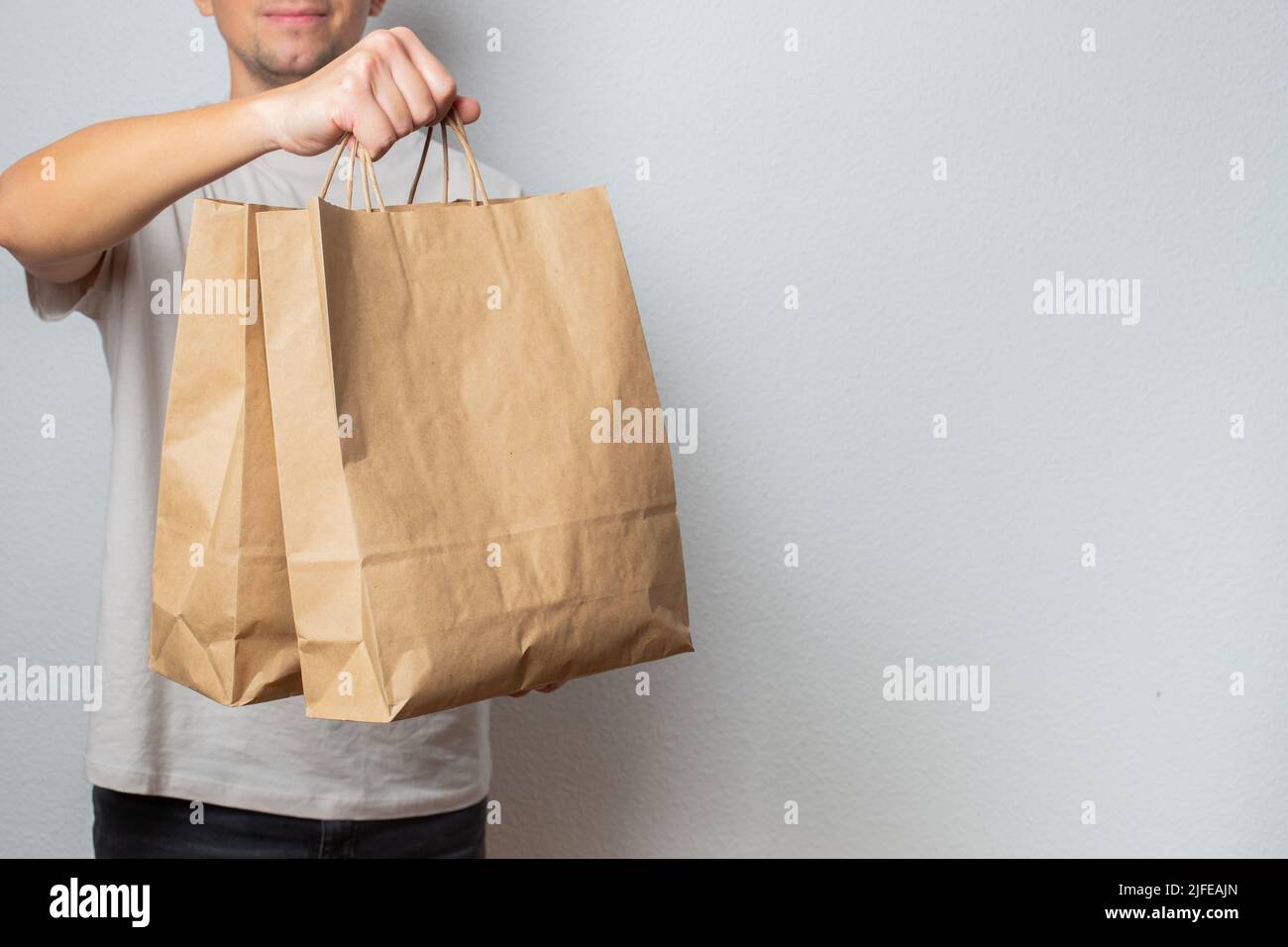 Lieferkonzept - schöner kaukasischer Liefermann, der eine Packtasche mit Lebensmitteln und Getränken aus dem Laden trägt. Isoliert auf grauem Studiohintergrund. Kopieren Stockfoto