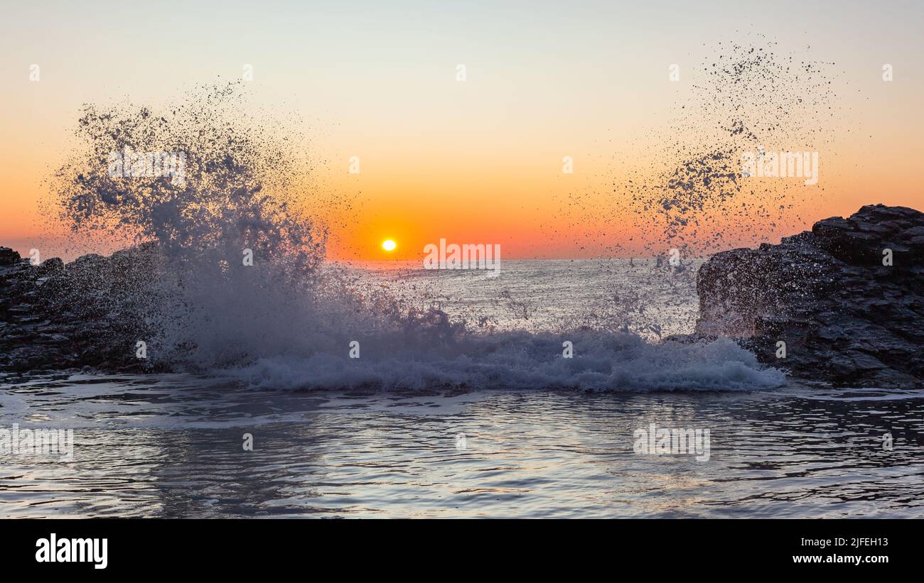 Dawn Beach felsiger Gezeitenpool mit Wellen-Sprühnebel gegen den Sonnenaufgang am Meereshorizont. Stockfoto