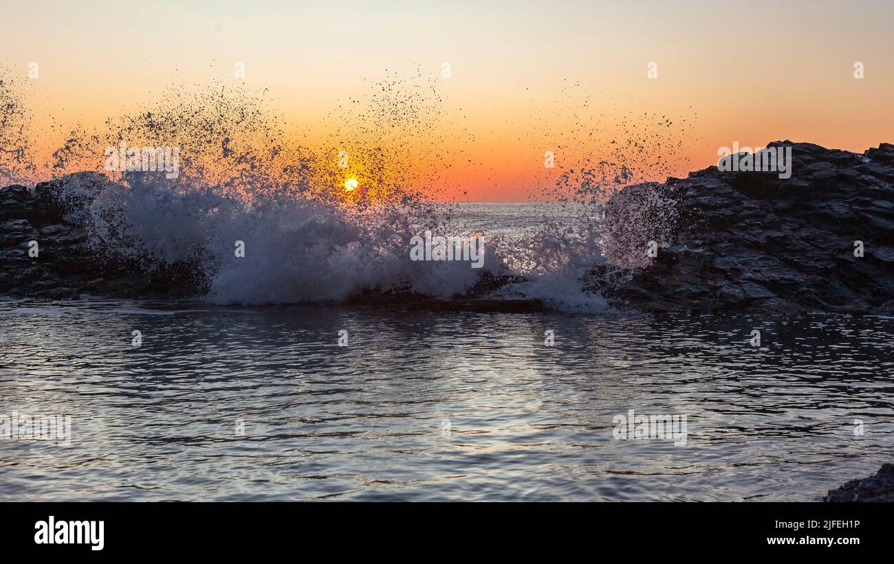 Dawn Beach felsiger Gezeitenpool mit Wellen-Sprühnebel gegen den Sonnenaufgang am Meereshorizont. Stockfoto