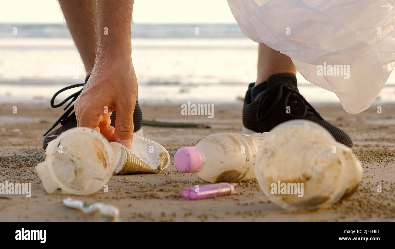 Nahaufnahme von männlichen Freiwilligen sammeln und sammeln Müll am Strand. Der Mann reinigt die Küste von Plastikmüll - Flaschen, Tassen. Freiwillige Stockfoto