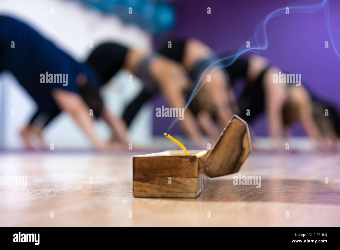 Eine Gruppe von Frauen, die im Yoga-Kurs nach unten posieren, mit Weihrauch im Vordergrund Stockfoto