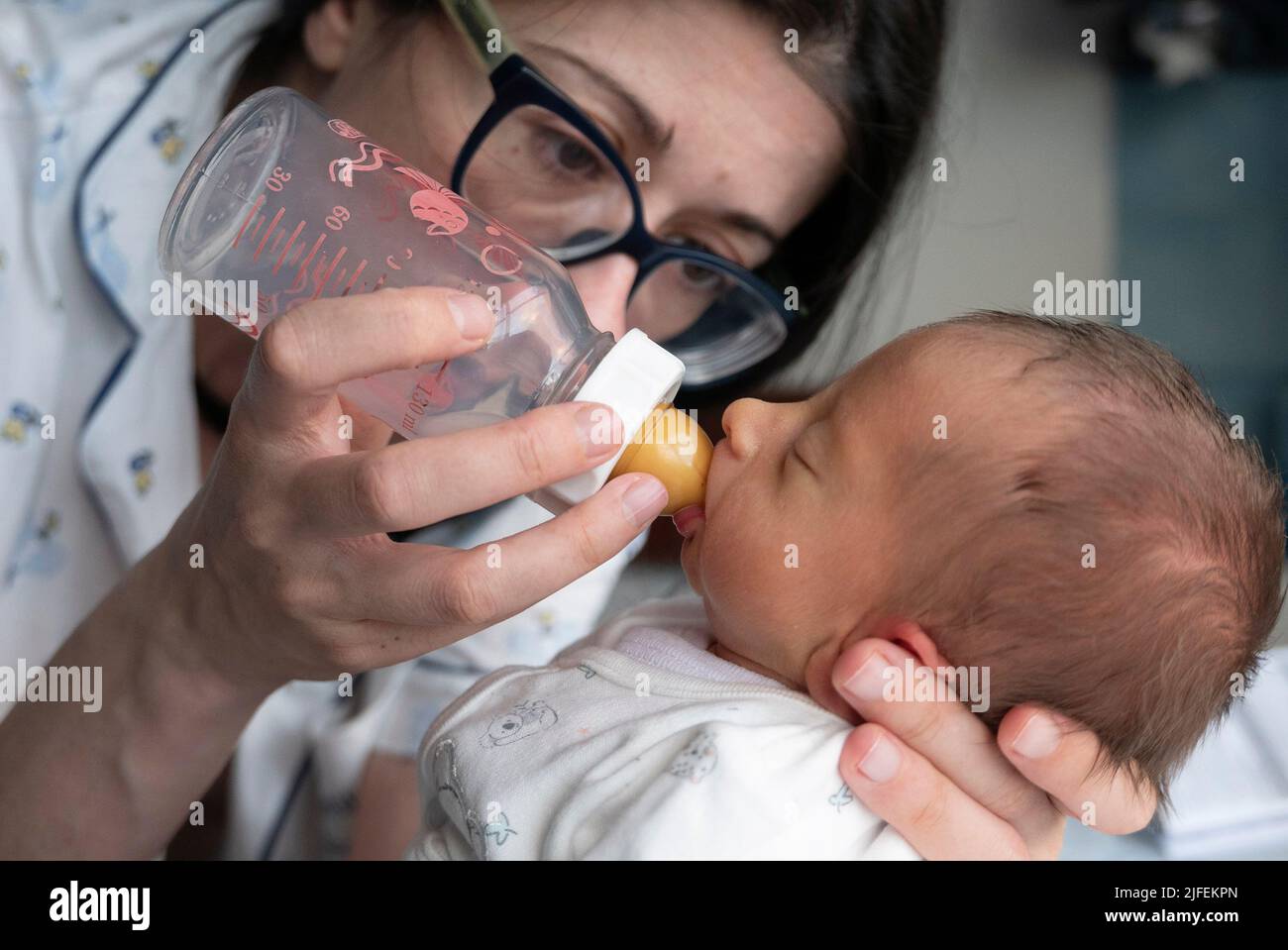 Junge Frau, die ein neugeborenes Frühgeborenes mit einer Stillflasche füttert Stockfoto