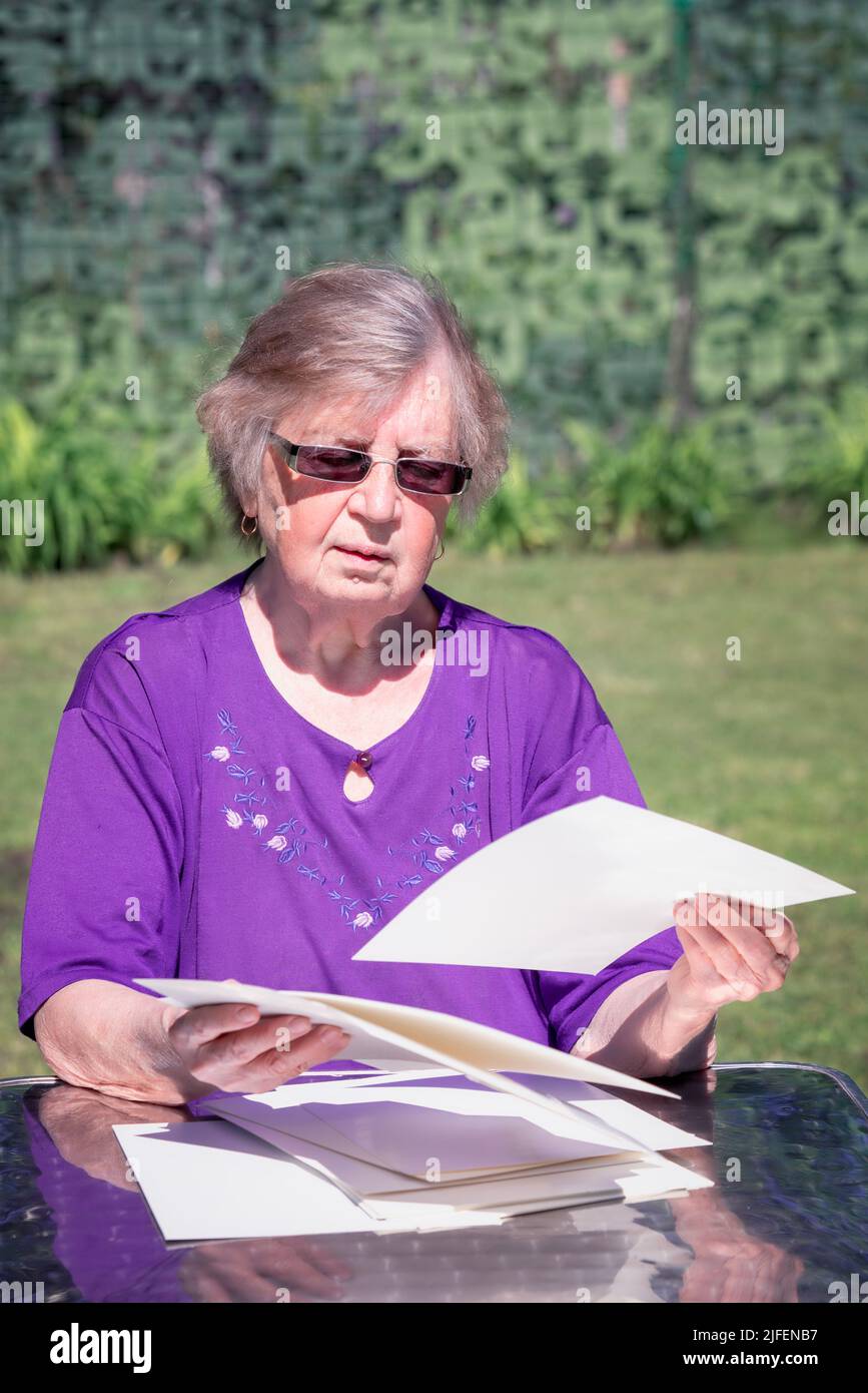 Ältere Frau, die im Freien sitzt und die Papiere durchsortiert. Stockfoto