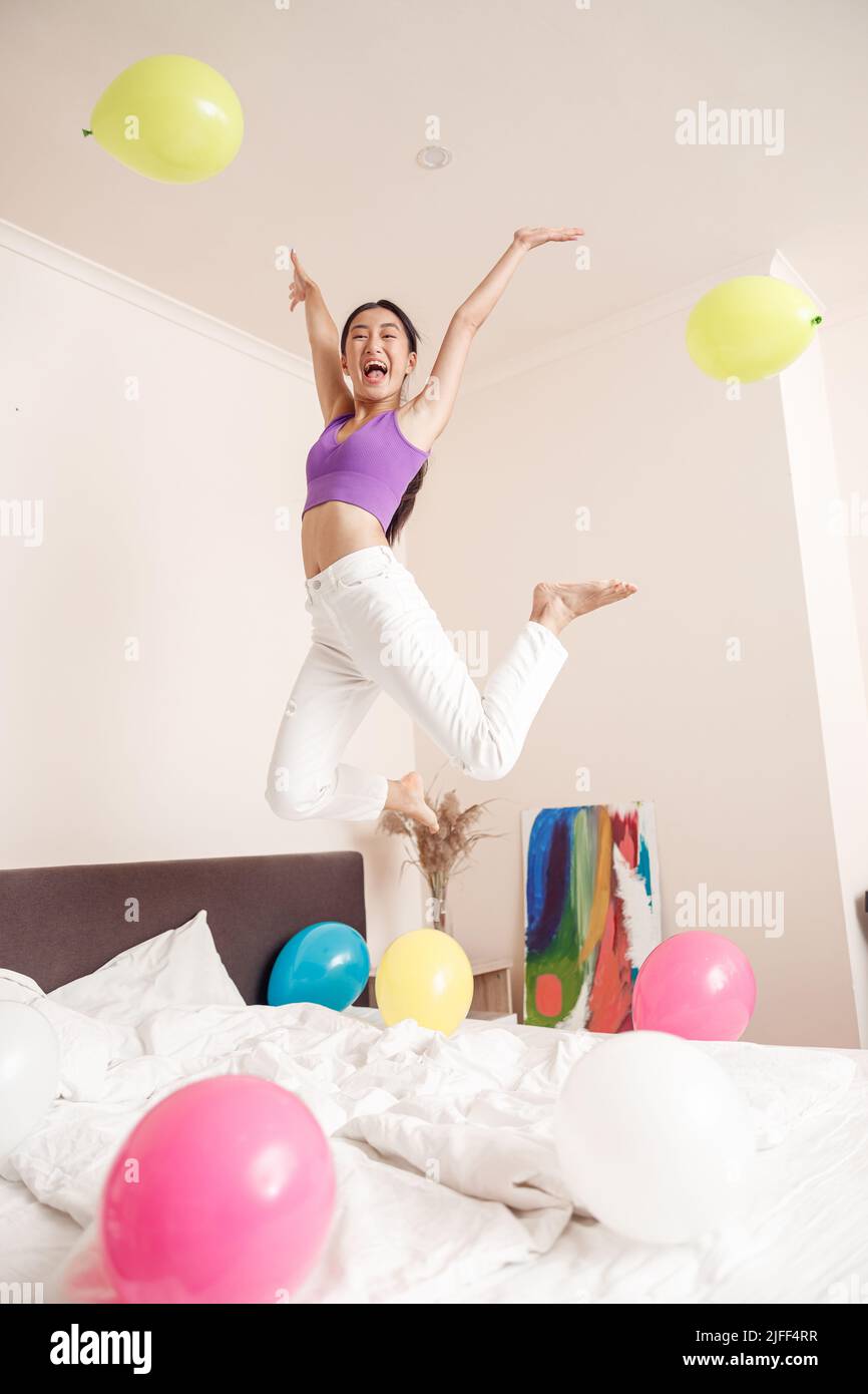 Fröhliche asiatische Frau springen im Schlafzimmer zu Hause Stockfoto