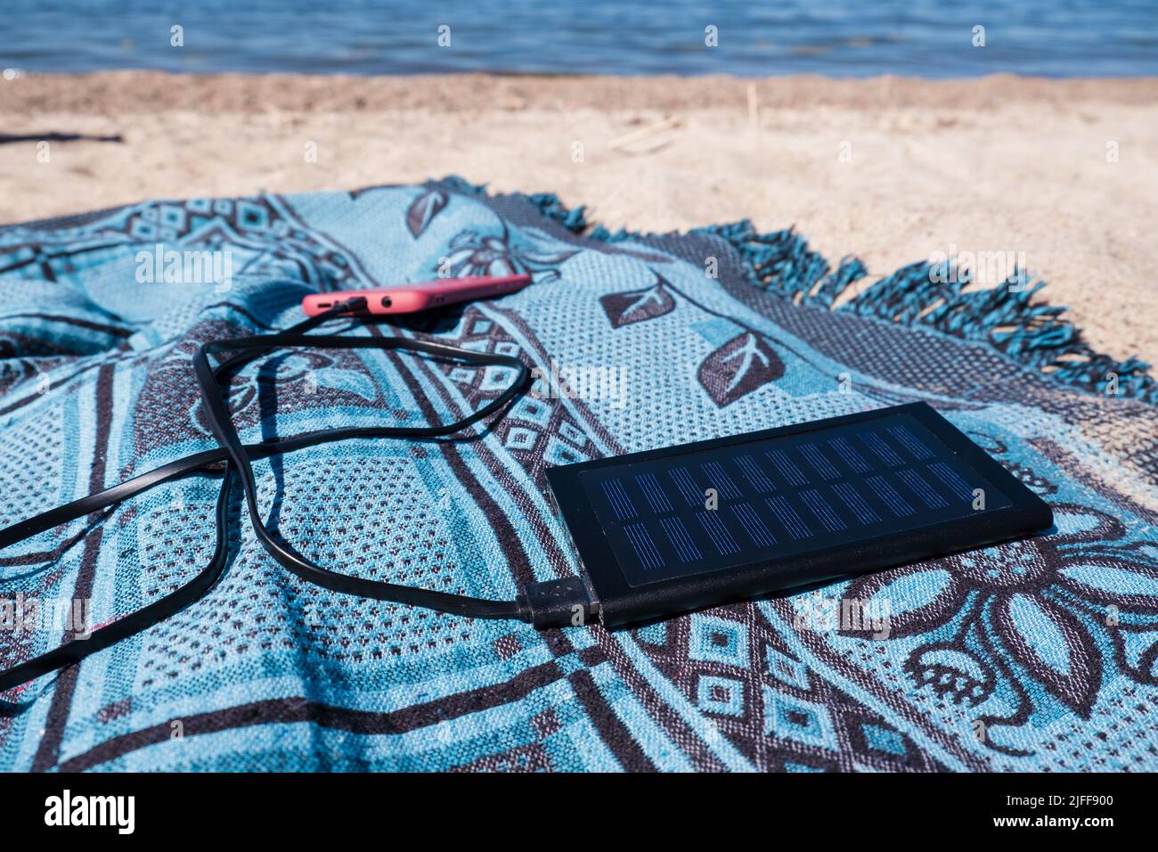 Solarpanel zum Aufladen eines Mobiltelefons am Strand. Tragbares Powerbank-Solarladegerät bei Sonneneinstrahlung. Sonnenenergie. Stockfoto