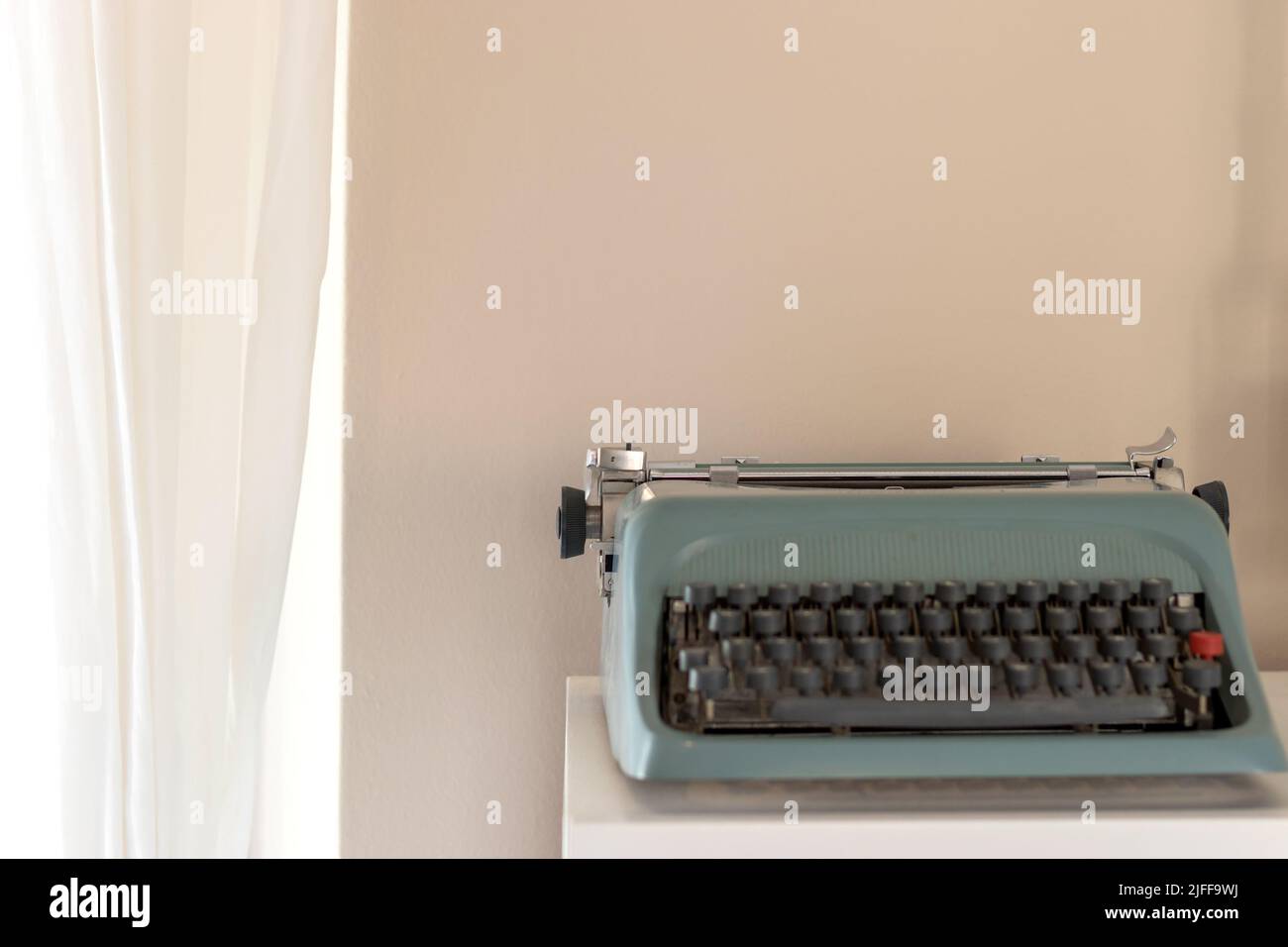 Schreibmaschine im Retro-Stil an beigefarbener Wand in der Nähe des Fensters in einem Raum mit Kopierraum. Weichfokus und unscharfe Tasten. Stockfoto