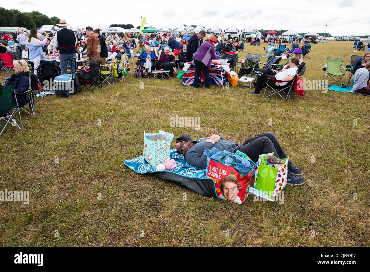 Woodstock, Oxfordshire, Großbritannien. 2.. Juli 2022. Mann liegt schlafend, umgeben von Einkaufstaschen. Einer mit Elf, der sagt: „Ich lächle einfach gerne“. Battle Prom Picknick-Konzerte. Blenheim Palace. Vereinigtes Königreich. Quelle: Alexander Caminada/Alamy Live News Stockfoto