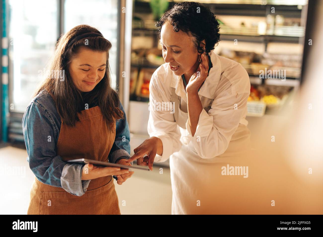 Zwei Supermarktmitarbeiter, die Online-Lebensmittelbestellungen auf einem digitalen Tablet verwalten. Ermächtigte Frau mit Down-Syndrom, die ein erfolgreiches kleines Unternehmen Witz Stockfoto